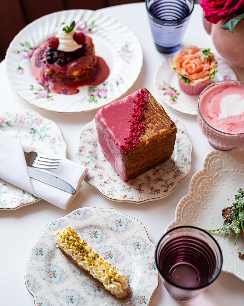 Een taart met roze glazuur, gebak en drankjes, uitgestald op een tafelkleed met bloemenmotief, vormen samen een heerlijk dessertbuffet in Halifax op Nova Scotia, Canada.