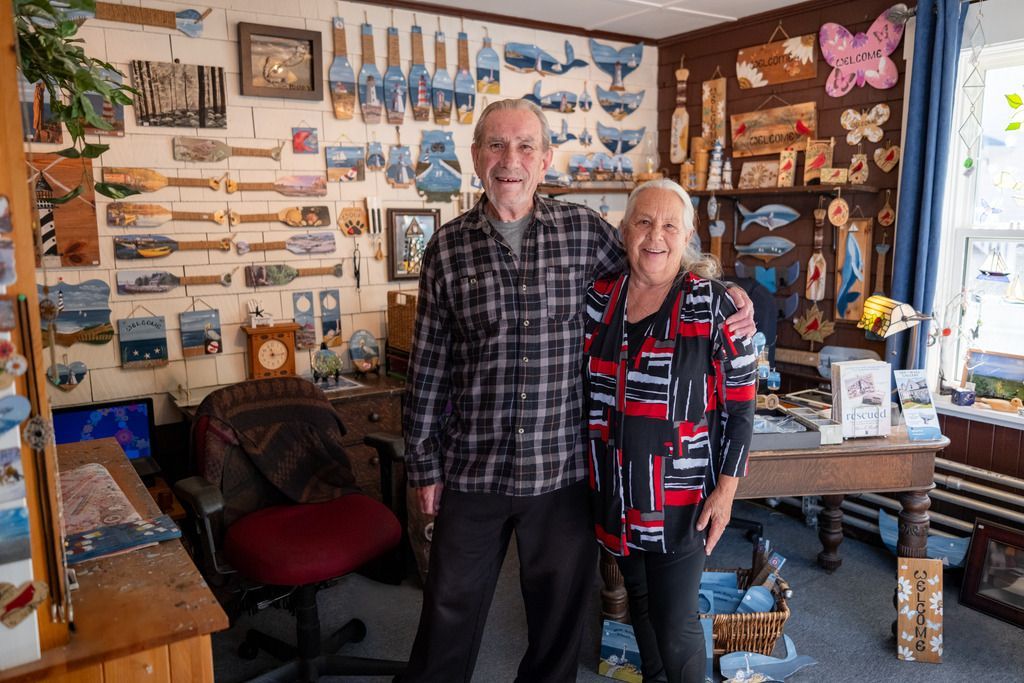 Twee mensen staan ​​in Digby op Nova Scotia in een gezellige, met kunst gevulde kamer met schilderijen, knutselwerkjes en een raam.