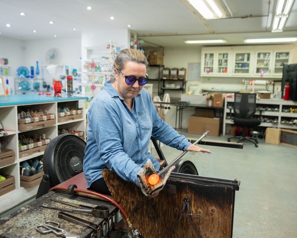 Een persoon die in een werkplaats in Peggy's Cove op Nova Scotia die aan het glasblazen is in de buurt van een werkbank en gereedschapsrekken.
