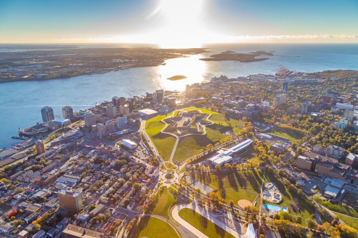 Luchtfoto van een stadspark in Halifax op Nova Scotia, Canada, aan het water bij zonsondergang, met kronkelende paden, nabijgelegen gebouwen en glinsterend water.