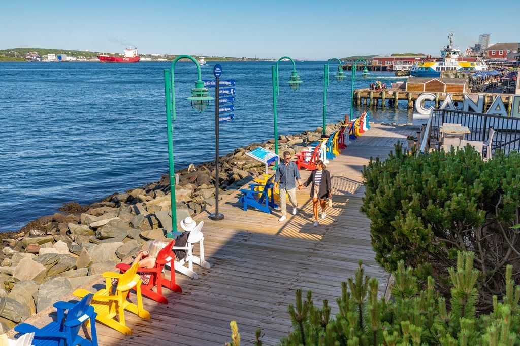 Een kleurrijke boulevard in Halifax op Nova Scotia, Canada, langs het water met bankjes, mensen en boten op een zonnige dag.