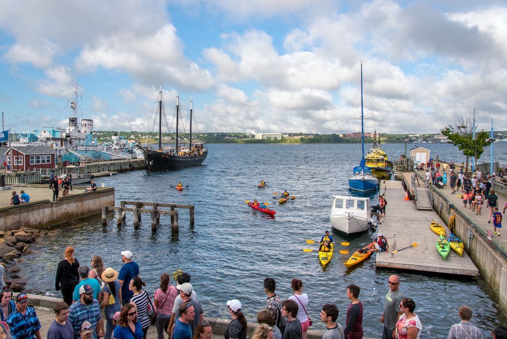Een drukke haven in Halifax op Nova Scotia in Canada met boten, kajaks en toeschouwers aan de waterkant onder een bewolkte hemel.