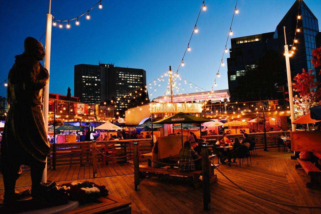 Een openluchtavondmarkt met lichtslingers, tafels en de skyline van de stad Halifax op Nova Scotia, Canada,op de achtergrond.