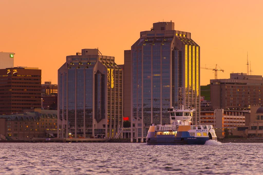 De havenskyline van Halifax op Nova Scotia, Canada, bij zonsondergang met hoge gebouwen en een veerboot op kalm water.