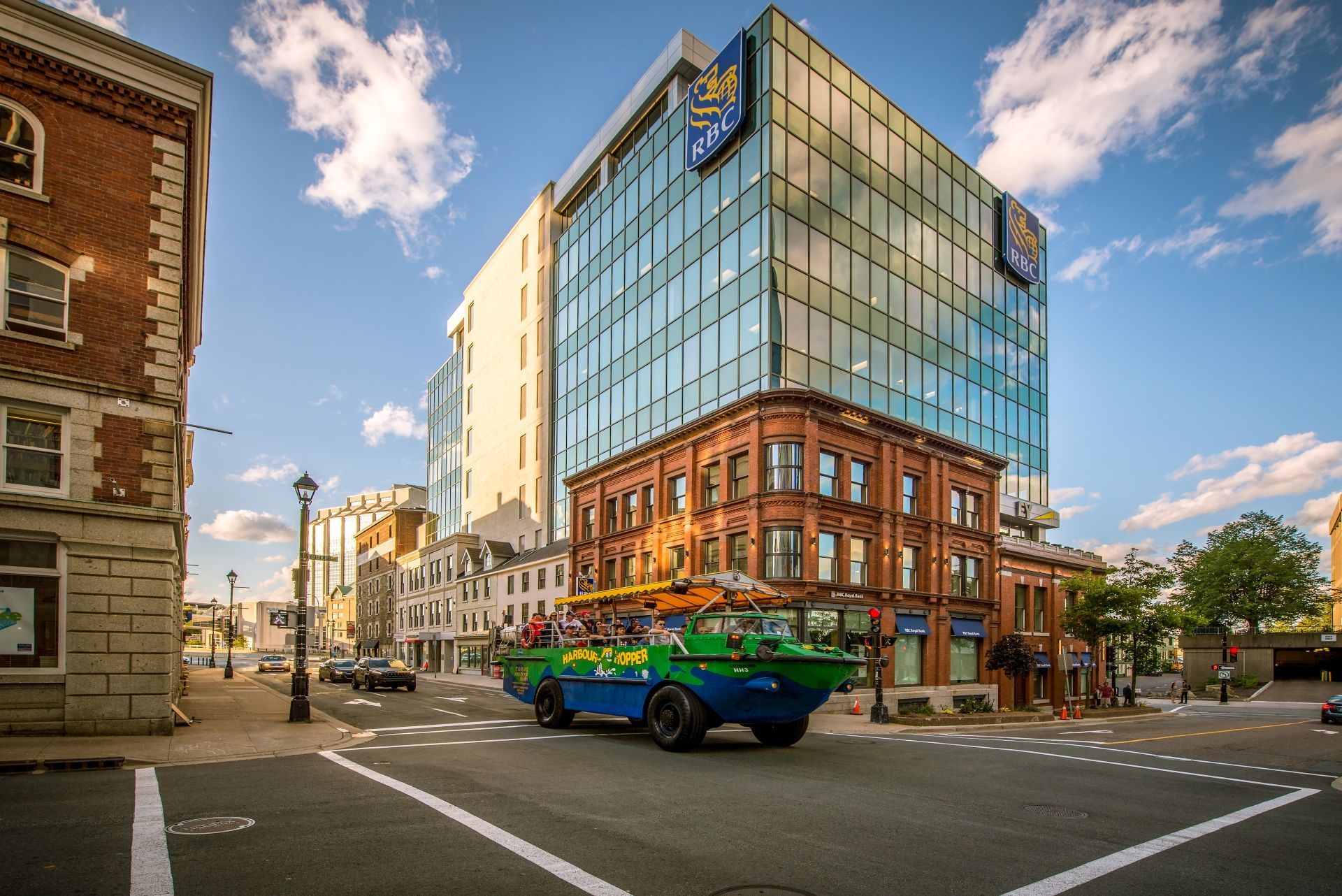 Modern glazen kantoorgebouw op een stadskruispunt in Halifax op Nova Scotia, Canada,met een kleurrijk amfibisch voertuig van Hopper Boat Tours en een blauwe hemel bij zonsondergang.