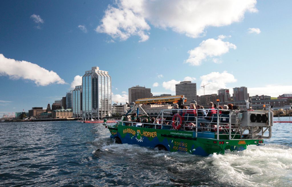 Een amfibisch voertuig van Hopper Boat Tours vaart over woelig water nabij de skyline van Halifax op Nova Scotia, Canada, onder een blauwe hemel.