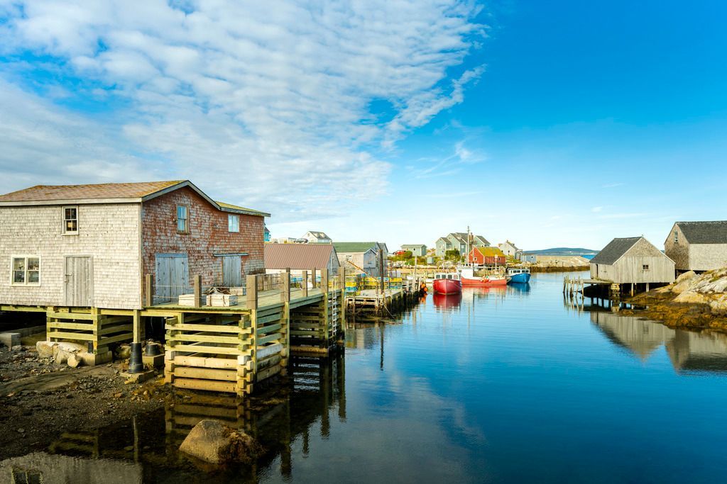 Kleurrijke huizen en boten aan het water in Peggy's Cove op Nova Scotia weerspiegelen zich in het kalme water onder een blauwe hemel.