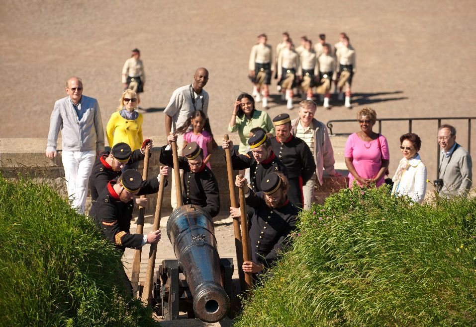 Mensen lopen met een groot, historisch kanon van de citadel van  Halifax op Nova Scotia, Canada, een grasheuvel op, met een groep achter hen aan.