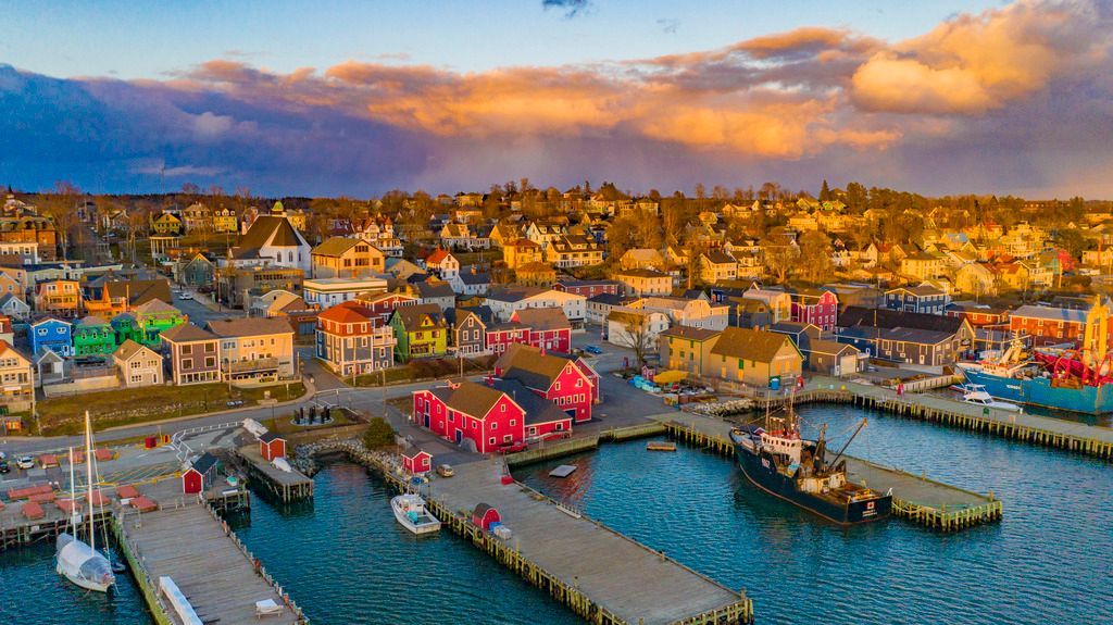 Het kleurrijke havenstadje Lunenburg op Nova Scotia bij zonsondergang met dokken, boten en gebouwen aan het water onder gloeiende wolken.