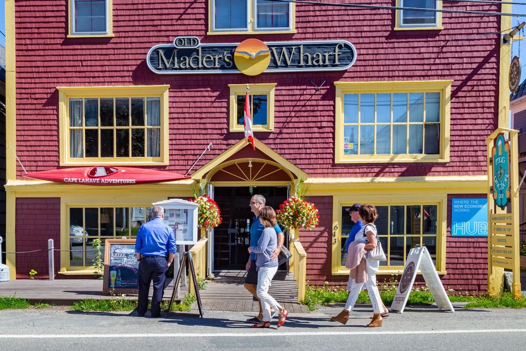 Mensen lopen langs een kleurrijke winkelpui in Mahone Bay, Nova Scotia, met een 