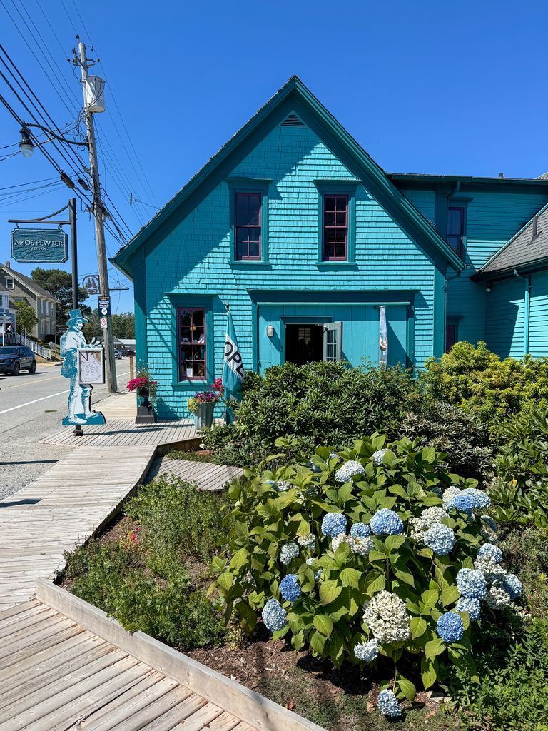 Een turquoise huis in Mahone Bay, Nova Scotia, in een zonnige straat met hortensia's en een houten vlonderpad.