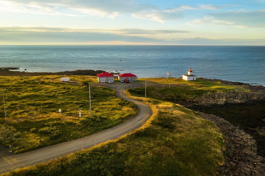 Een kustpad leidt naar rode huisjes en de witte vuurtoren Grand Passage Lighthouse op Brier Island, Nova Scotia,op een grasrijke klif met uitzicht op zee.