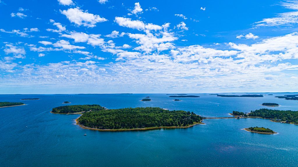 Luchtfoto van het weelderige groene eiland Oak Island, Nova Scotia, in een blauwe oceaan onder een heldere hemel met verspreide wolken.