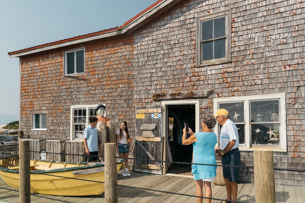 Mensen staan ​​buiten een verweerd houten gebouw op een kade aan het water in Peggy's Cove op Nova Scotia.