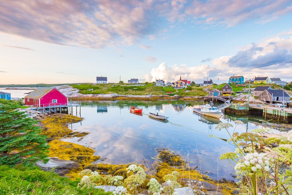 Het kleurrijk dorpje Peggy's Cove op Nova Scotia aan de oceaan met huizen die weerspiegeld worden in het kalme water onder een gedeeltelijk bewolkte hemel.