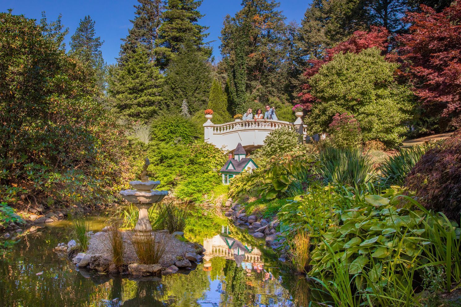 De kleurrijke tuinen van de Public Garden van Halifax op Nova Scotia, Canada, met een vijver, een stenen fontein en weelderige bomen rondom een ​​klein wit huisje.