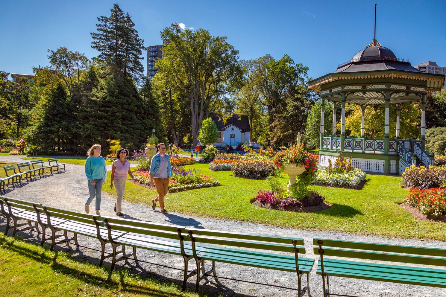 Mensen wandelen door een zonnige bloementuin naast een prieel en bankjes van de Public Gardens van  Halifax op Nova Scotia, Canada..