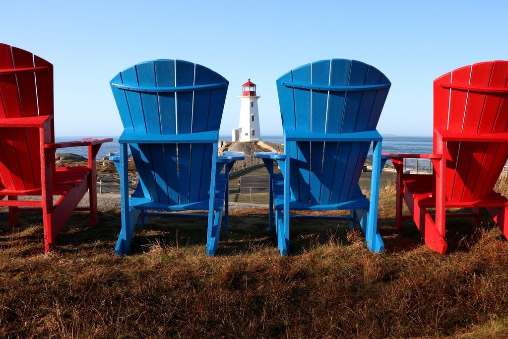 Rode en blauwe strandstoelen met uitzicht op de oceaan en de vuurtoren van Peggy's Cove op Nova Scotia in de verte.
