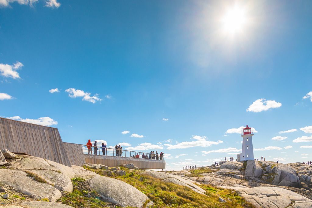 Mensen op een rotsachtig strand bij de vuurtoren van Peggy's Cove op Nova Scotia vuurtoren onder een helderblauwe hemel.
