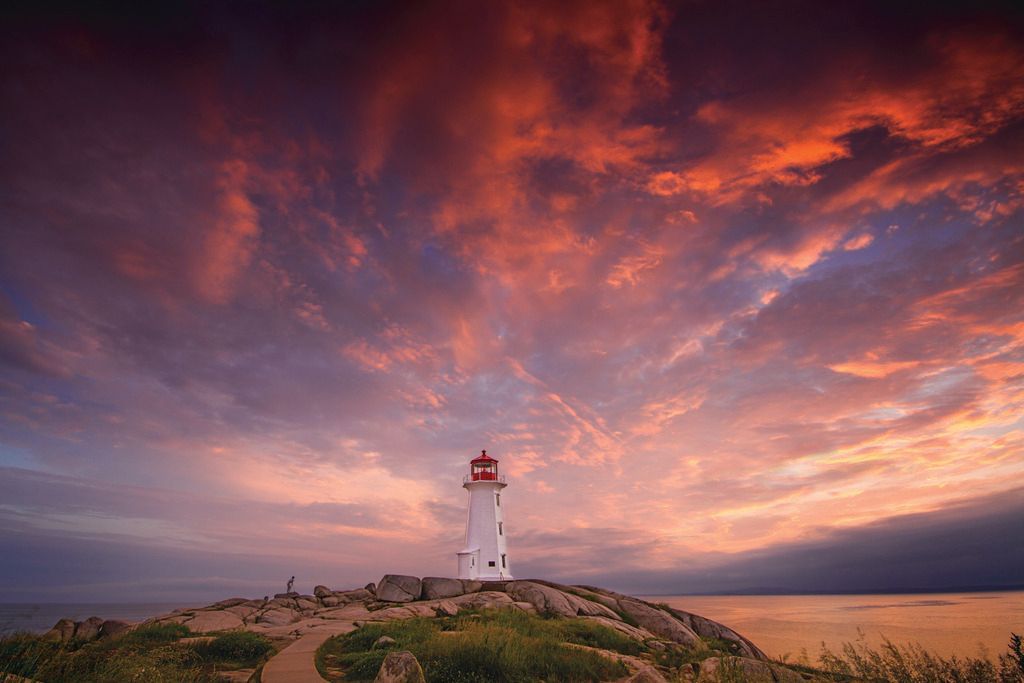 De vuurtoren van Peggy's Cove op Nova Scotia op een rotsachtige kust bij zonsondergang, onder dramatische paars-oranje wolken.