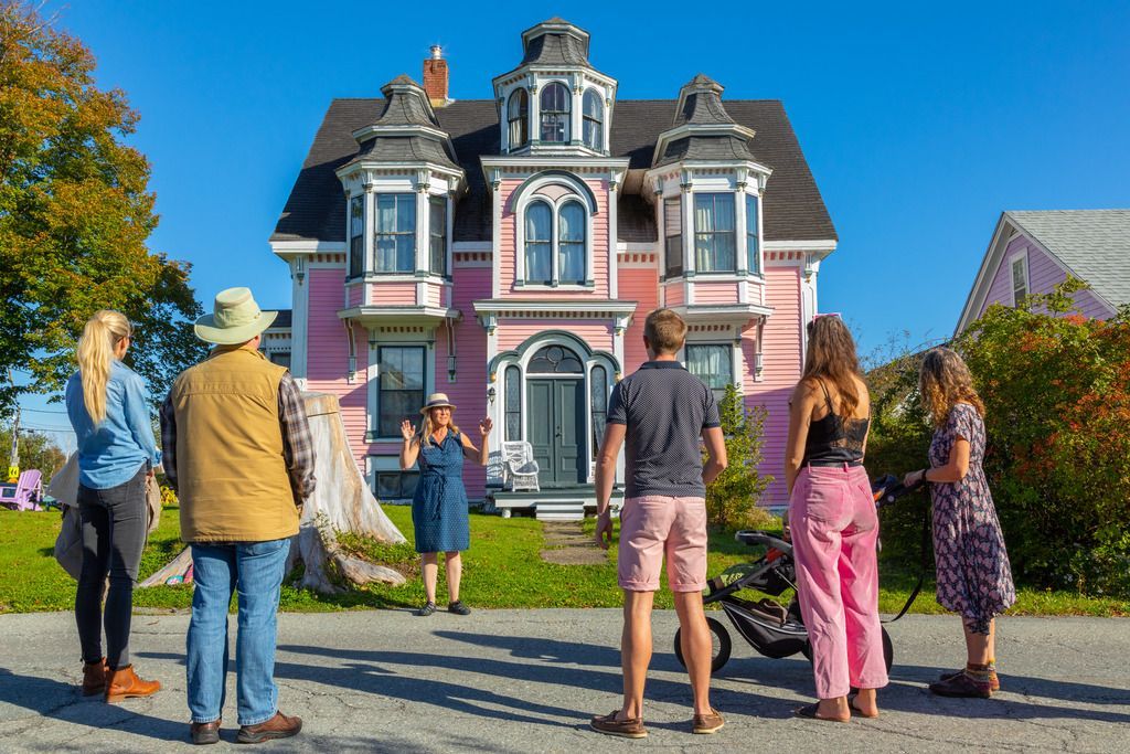 Een groep mensen staat op straat tegenover een kleurrijk Victoriaans huis in Lunenburg, Nova Scotia in het heldere daglicht.