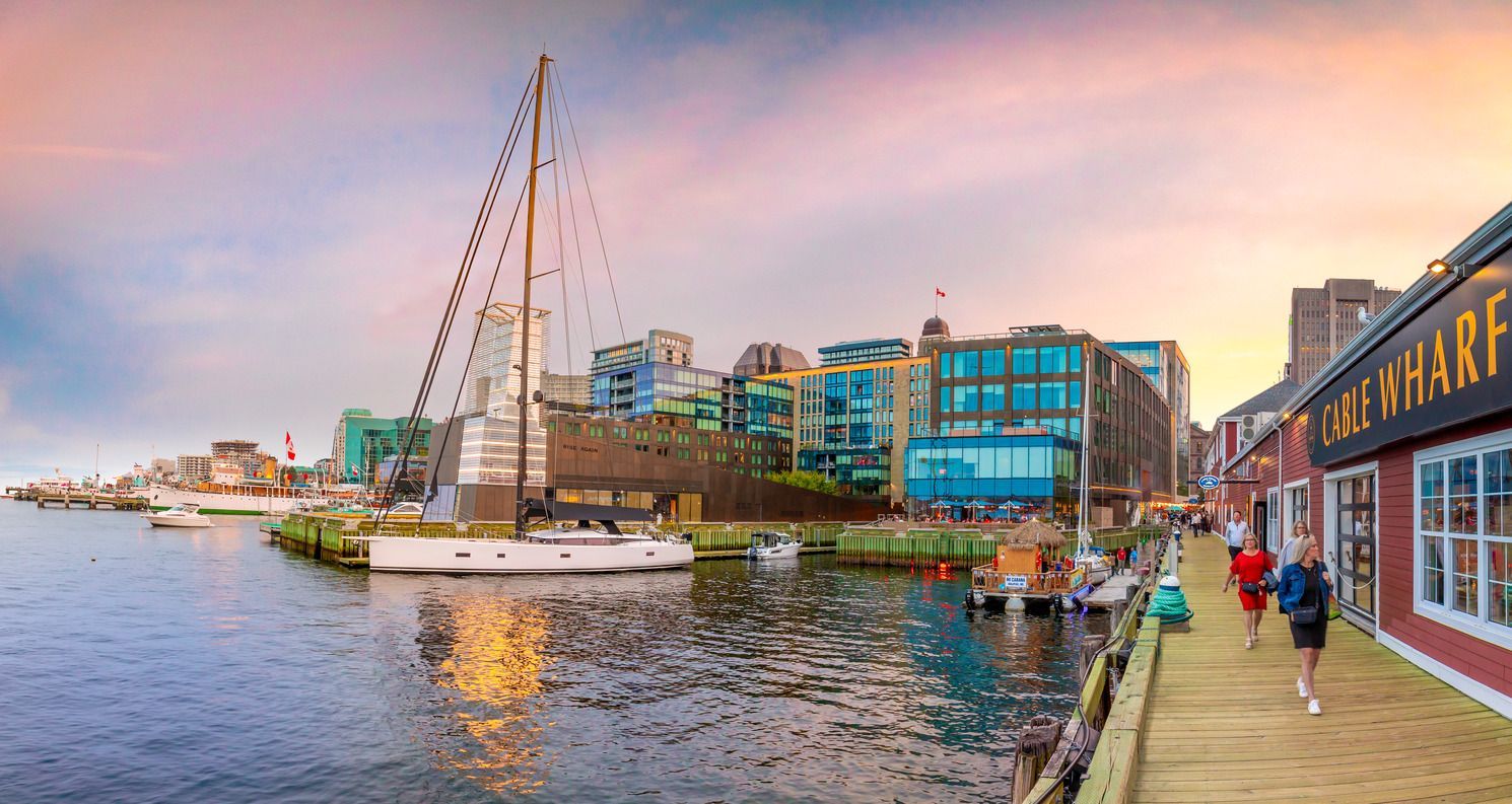 Haven van Halifax op Nova Scotai, Canada, met aangemeerde zeilboten naast kleurrijke gebouwen aan het water en een promenade langs de kade bij zonsondergang.