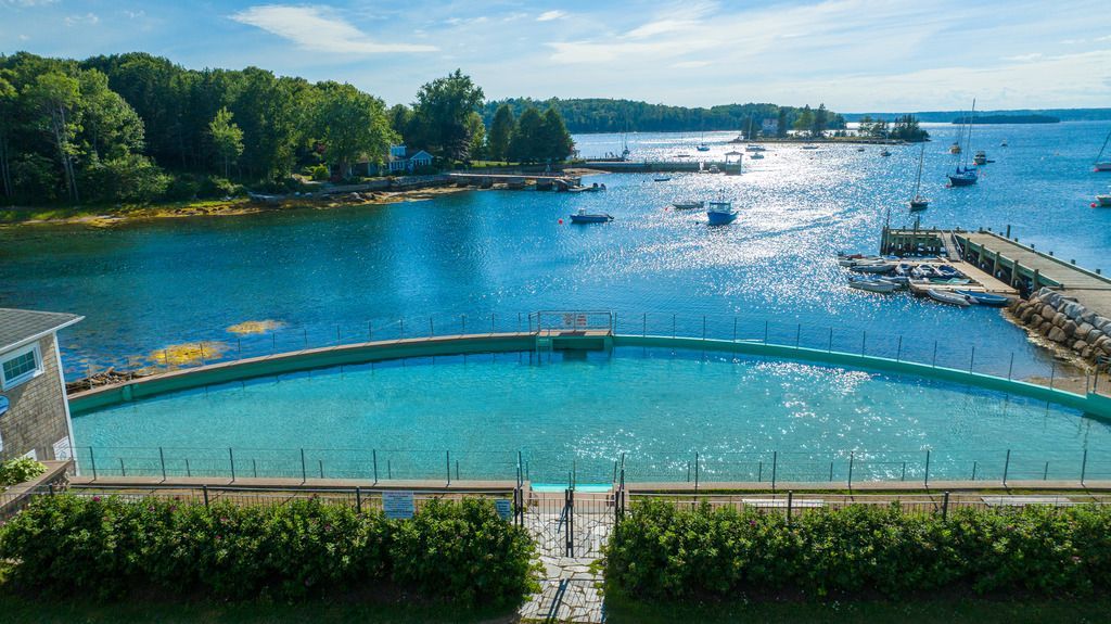 Zonnige kusthaven van Chester op Nova Scotia met blauw water, golfbrekers, zeilboten en bomen langs de oever.