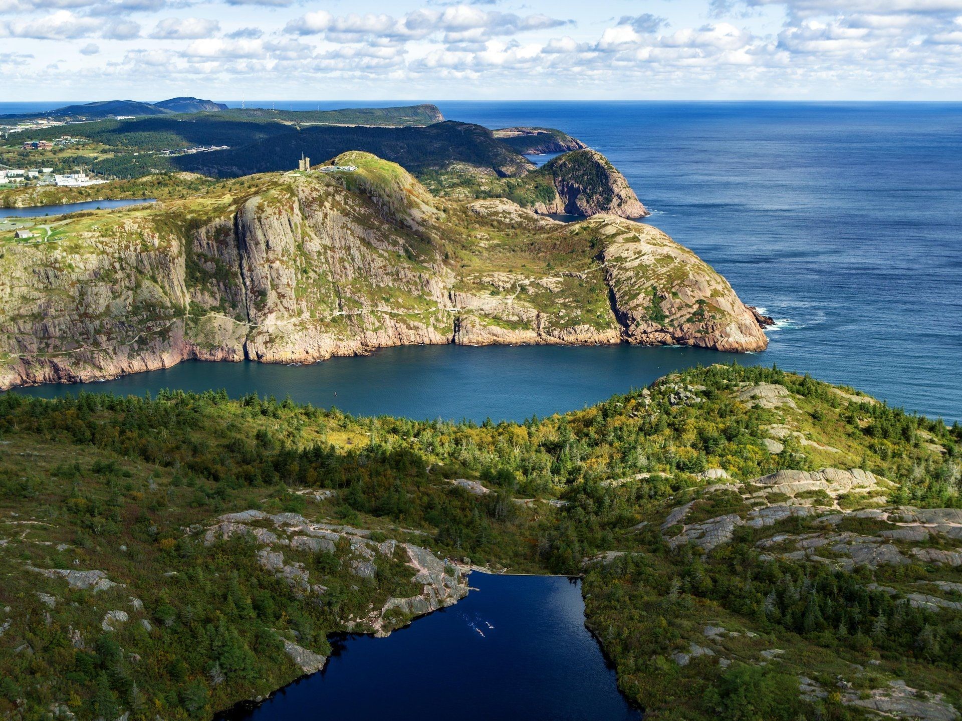Groene kustkliffen en een blauwe oceaan met een kleine lagune onder een gedeeltelijk bewolkte hemel in de omgeving van Signal Hil in St. John's Newfoundland..