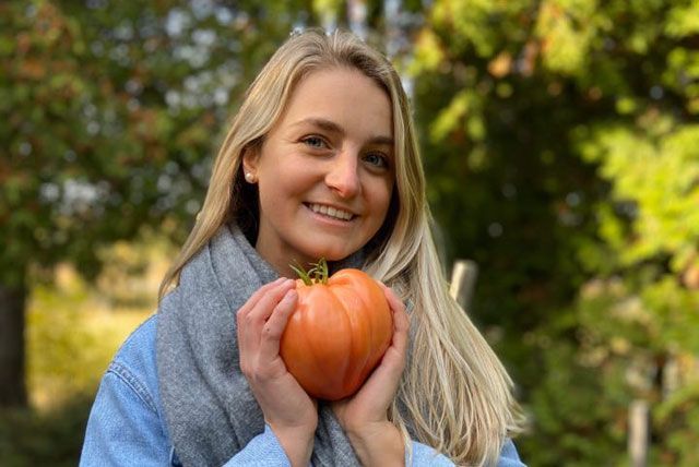 Lachende persoon die een kleine oranje pompoen vasthoudt in de buitenlucht, midden herfstbladeren