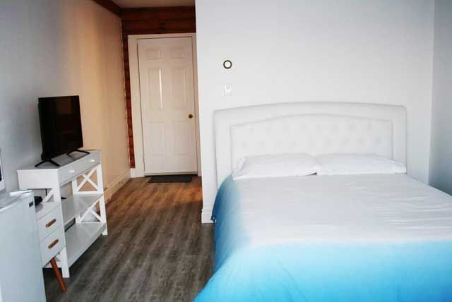 Kleine slaapkamer met een wit bed, een tv op een standaard en een vloer met houtlook.
