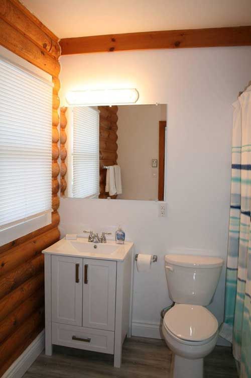 Kleine, rustieke badkamer met witte wastafel, spiegel, toilet en blauwgestreept douchegordijn.