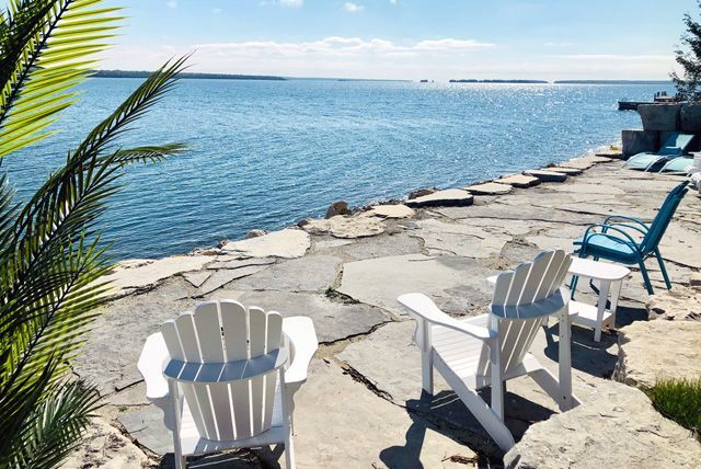 Witte stoelen op een rotsachtig terras aan zee met uitzicht op kalm blauw water.