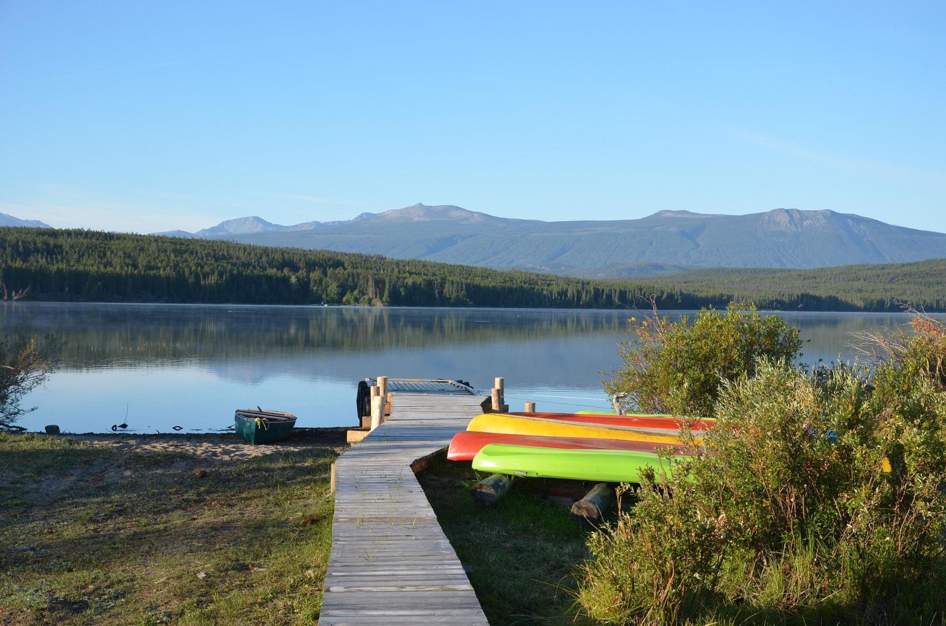 Leg aan bij een rustig meer met kleurrijke kajaks, beboste bergen en een helderblauwe hemel.