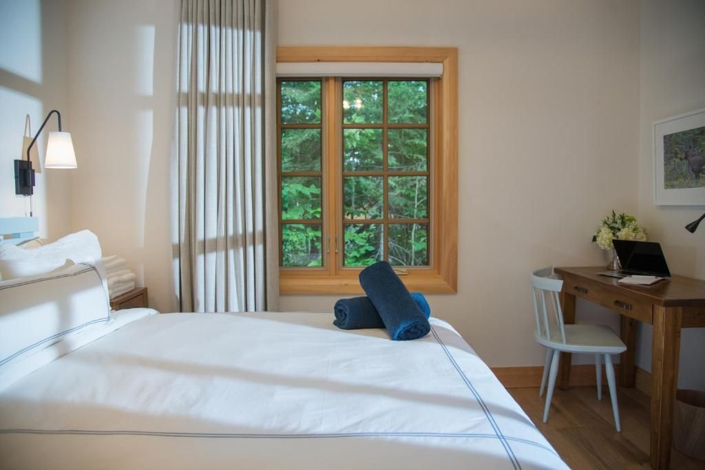 Lichte slaapkamer met wit bed, blauwe handdoek, houten raam en bureau tegen de muur.