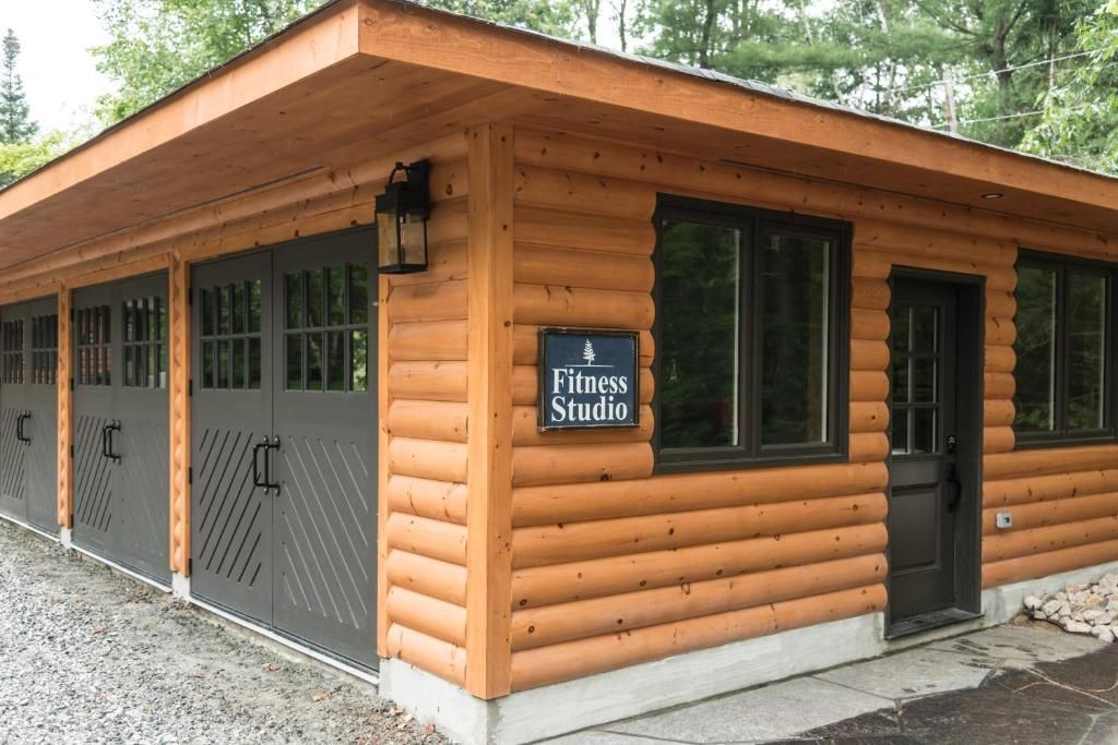 Een blokhutachtig gebouw met houten gevelbekleding, een overdekte veranda en garagedeuren, gelegen in een bosrijke omgeving.