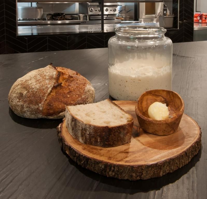 Brood, een sneetje brood, boter en een potje boter op een houten plank op het aanrecht.