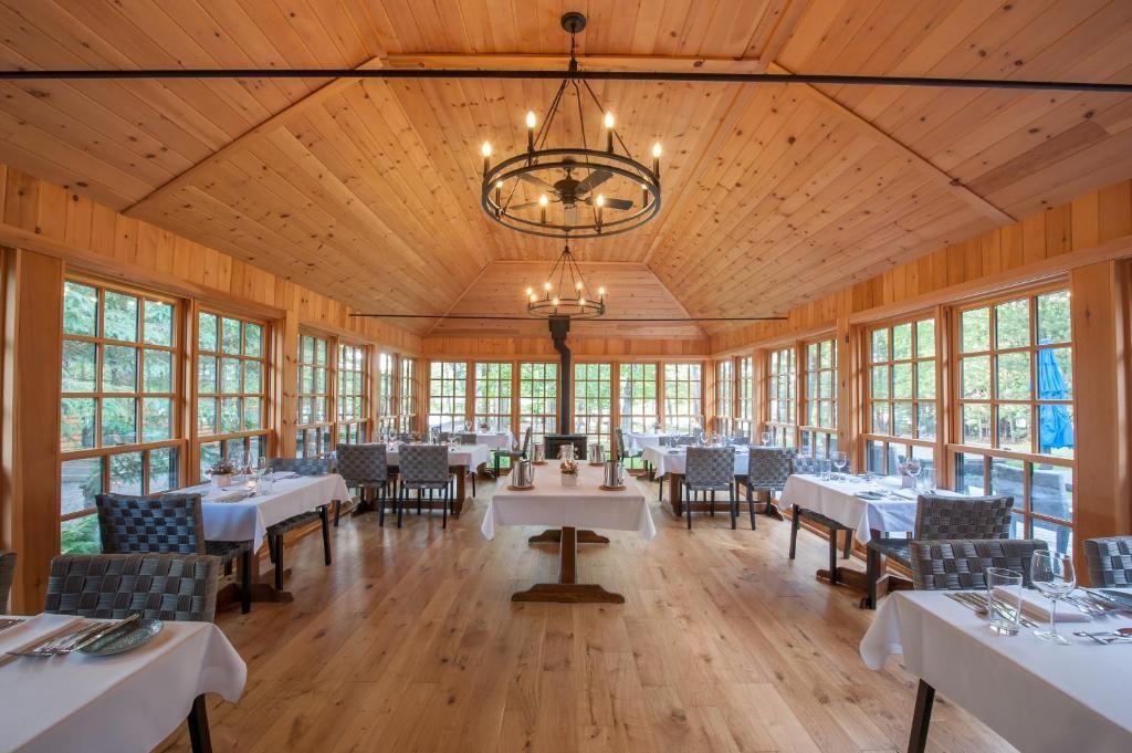 Een feestzaal met houten lambrisering, gedekte tafels, wit linnen en kroonluchters bij grote ramen.
