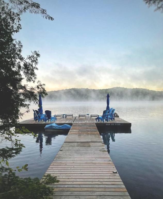 Een houten steiger die bij zonsopgang een mistig meer in steekt, met blauwe stoelen en een kalm, spiegelend wateroppervlak.