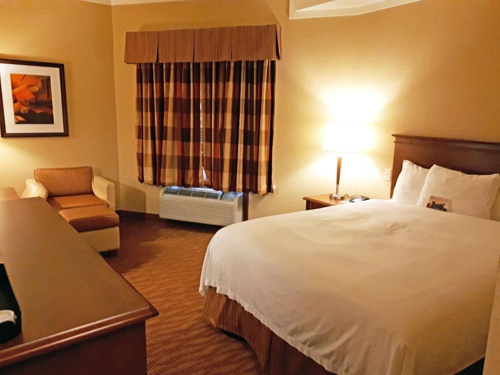 Hotelkamer met twee bedden, een stoel bij het raam en een lamp op een sfeervol verlicht nachtkastje.