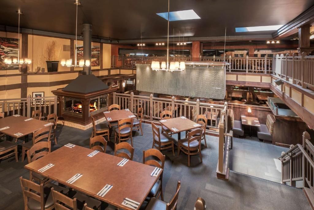 Lege restaurantzaal met houten tafels, stoelen, zitjes en warme verlichting.