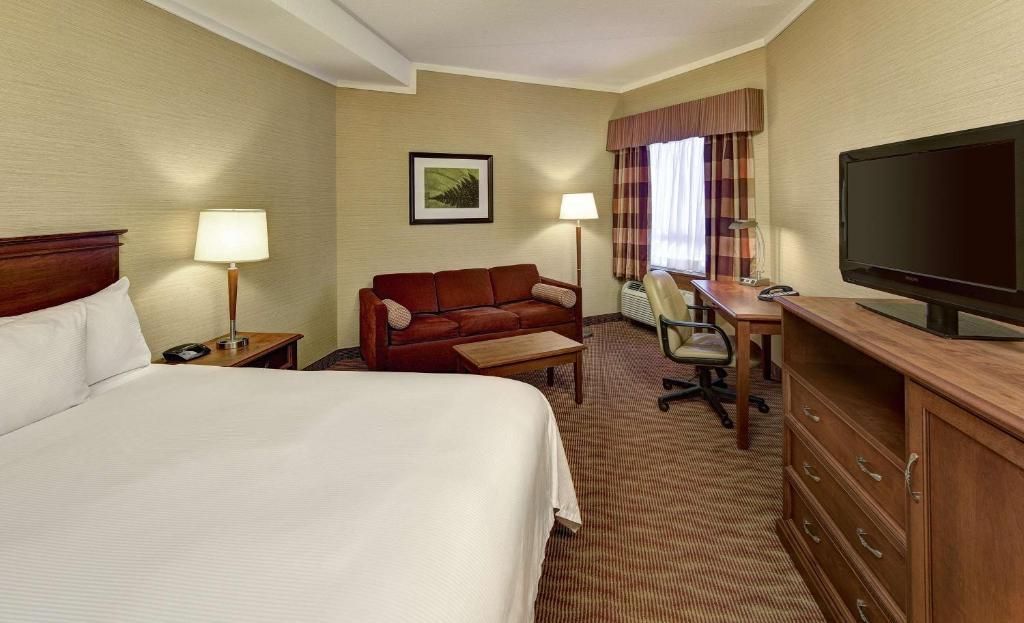 Hotelkamer met een bed, commode, tv, bureau en twee stoelen bij een raam met lamp.