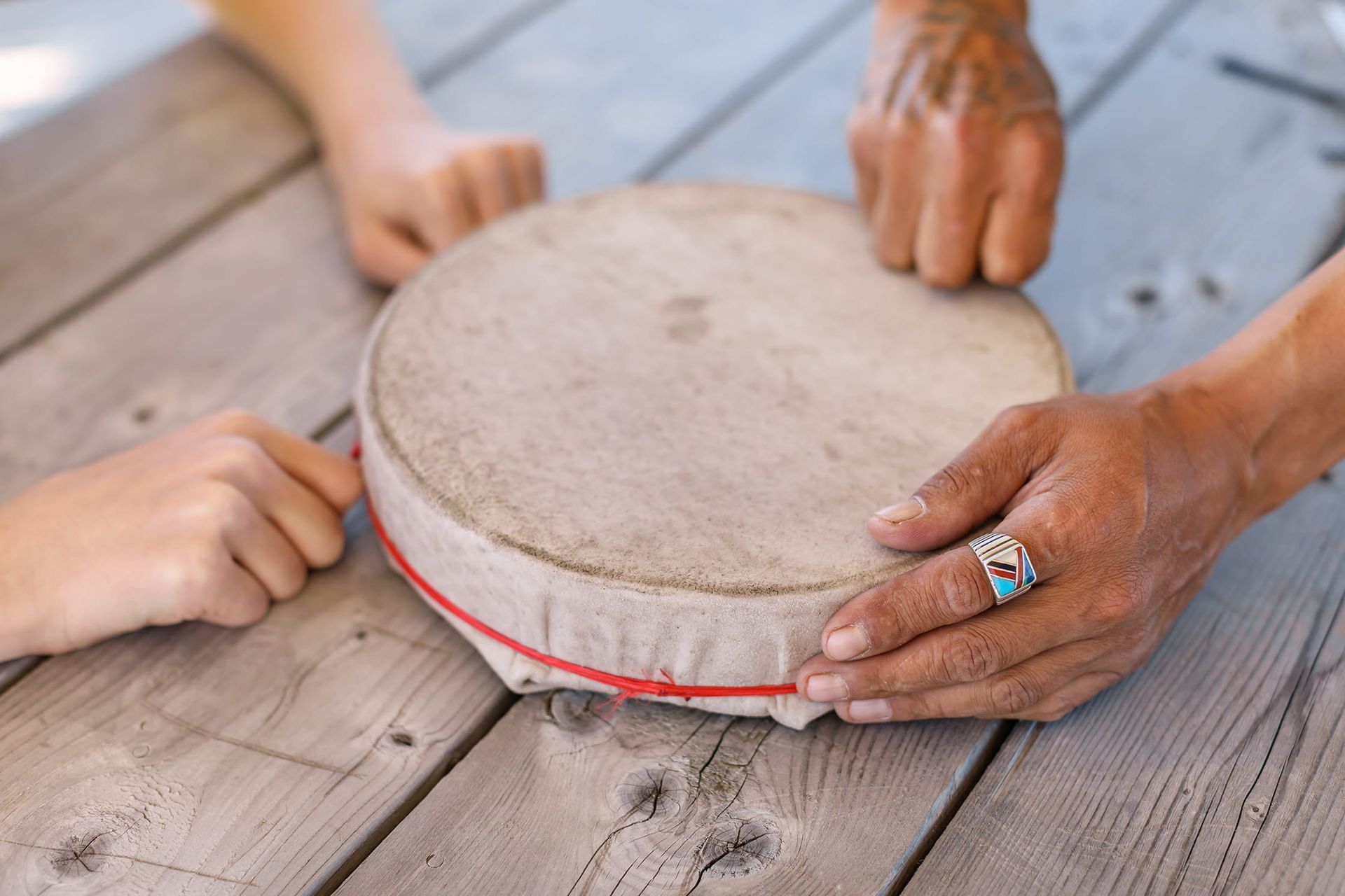 Handen houden een kleine ronde trommel vast op een verweerde houten tafel.