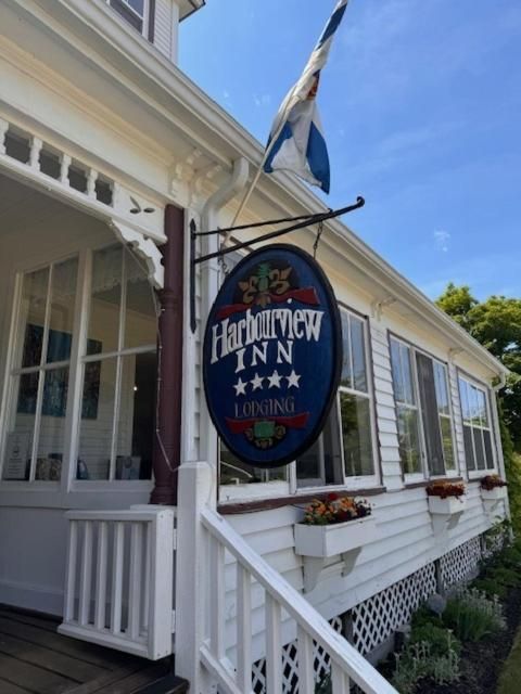 Het uithangbord van Harbouview Inn hangt aan een witte veranda onder een blauwe hemel.