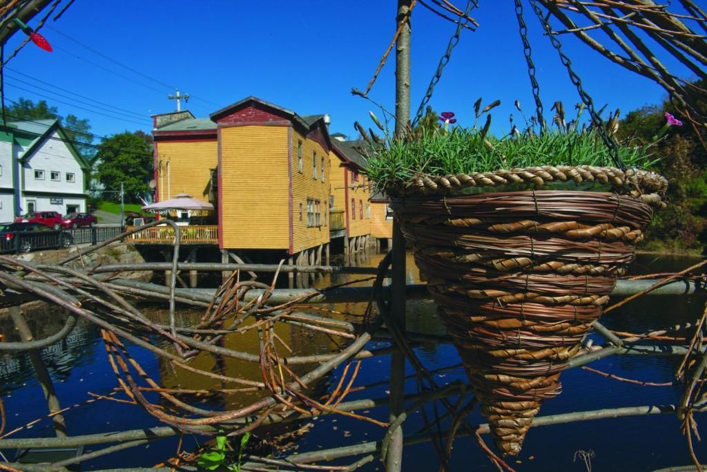 Haventafereel met geweven, mandvormige visvallen, gele gebouwen en zeilbootmasten aan kalm water.