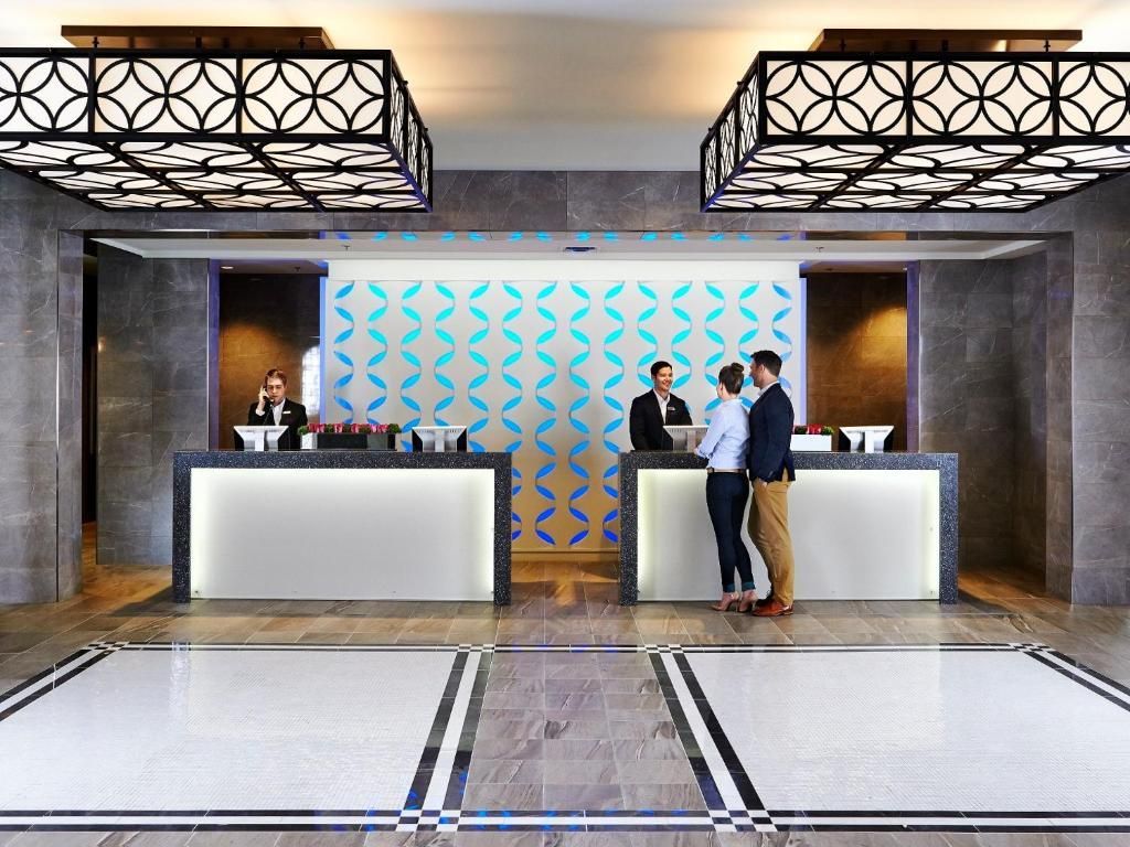 Moderne hotelreceptie van The Prince George Hotel, Halifax met twee witte balies, een muur met patroon en twee medewerkers die een gast helpen.