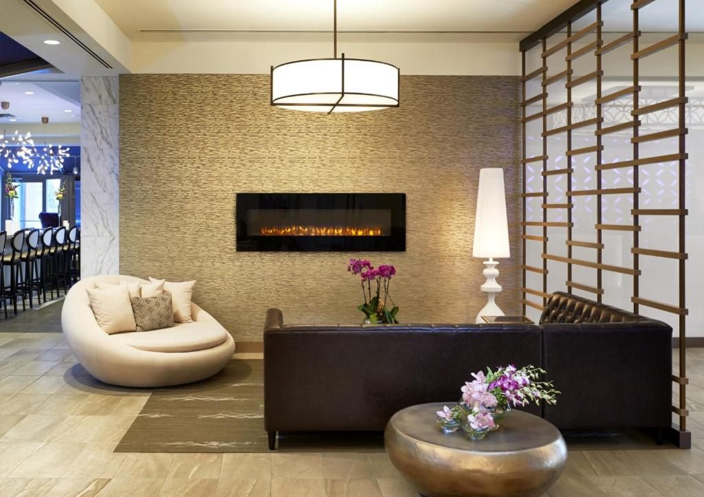 Moderne hotellobby van The Prince George Hotel, Halifax met beige muren, donkere bank, ronde stoel, open haard, hanglamp en houten scheidingswand.