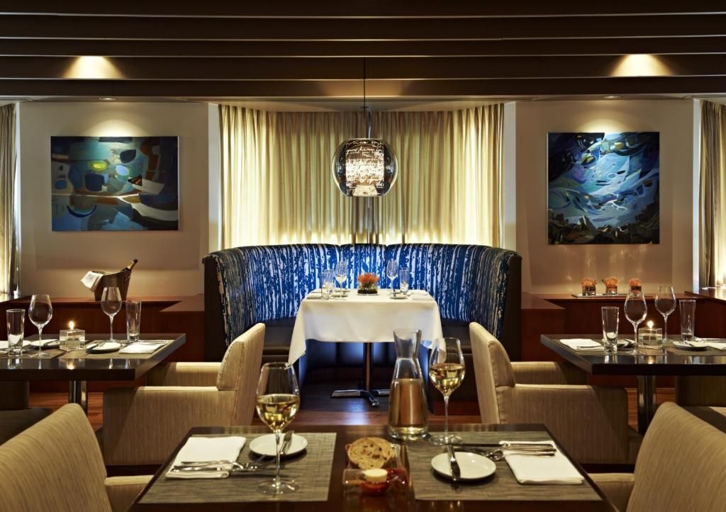 De elegante restaurantzaal van The Prince George Hotel, Halifax met gedekte tafels, warme verlichting en blauwe fluwelen banken.