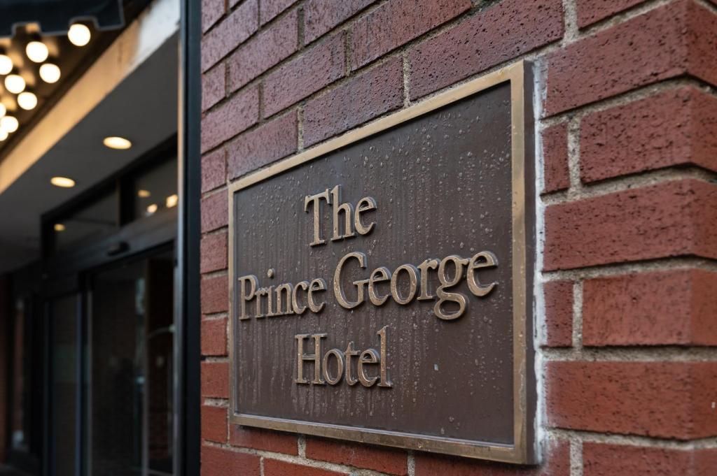 Het uithangbord van het Prince George Hotel op een bakstenen muur naast een gebouwingang.