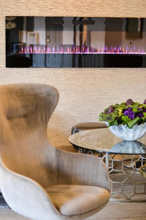 Moderne lounge van The Prince George Hotel, Halifax met beige fauteuil, ronde marmeren tafel, bloemstuk en aan de muur gemonteerde open haard.