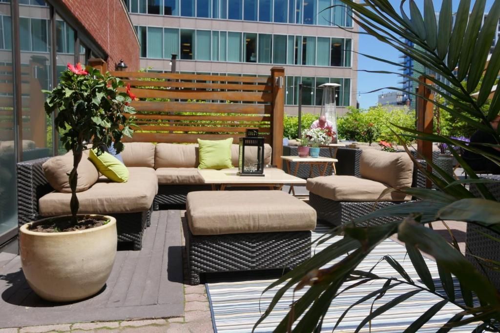 Buitenterras van The Prince George Hotel, Halifax met beige zitmeubelen, een houten pergola, potplanten en moderne appartementengebouwen op de achtergrond.